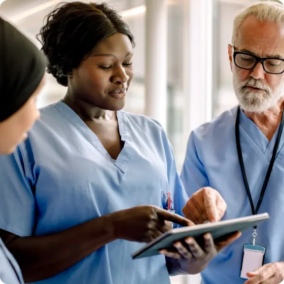 三位医疗保健专业人员正在看着平板电脑并讨论它。